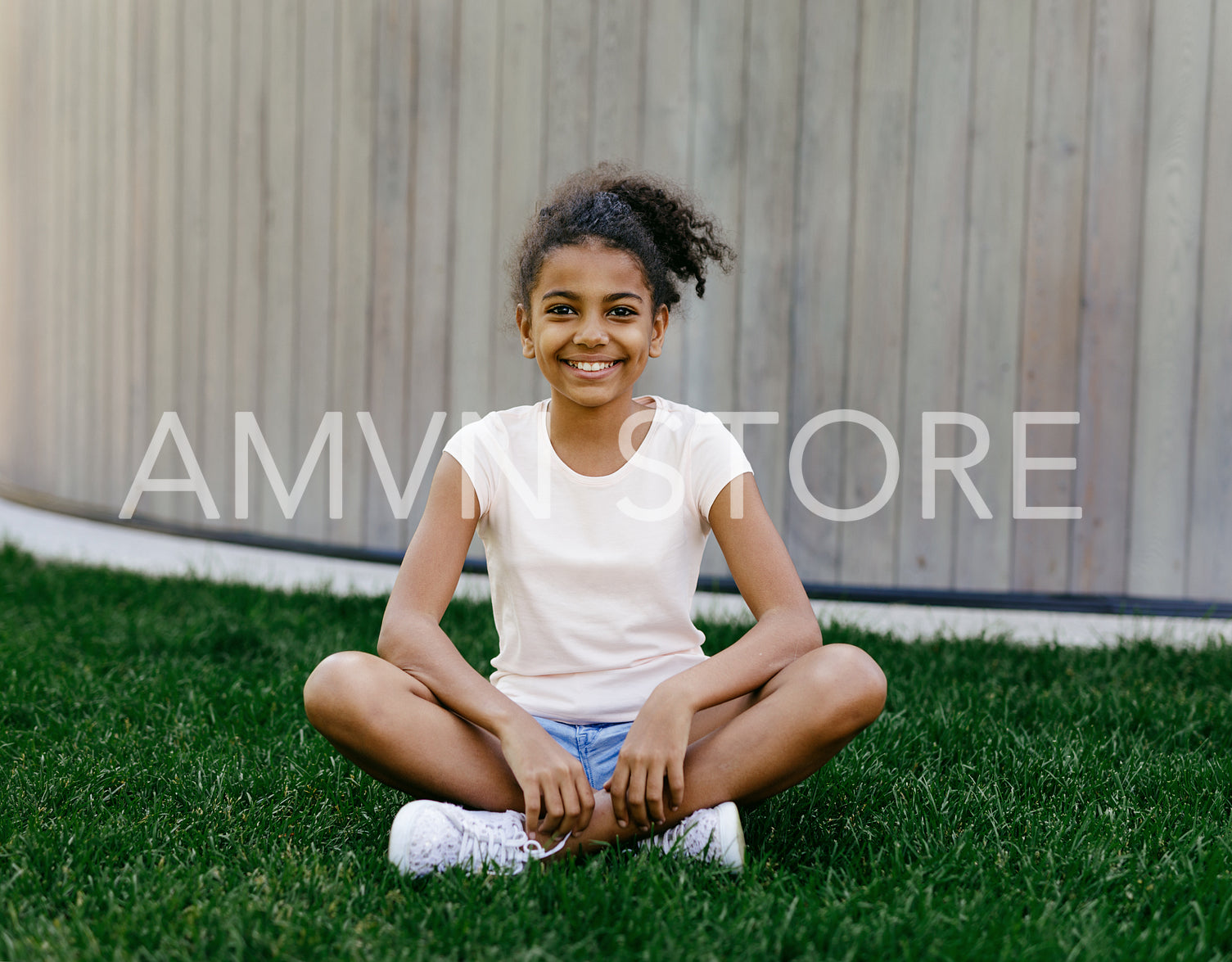 Portrait of a smiling girl sitting on the grass, looking at camera	