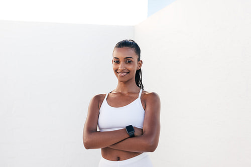 Portrait of a smiling woman in sportswear with crossed arms. Confident female athlete looking at camera outdoors.