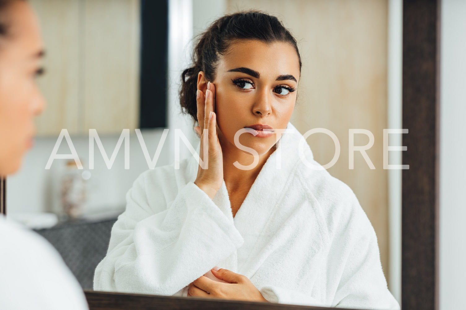 Young woman applying face cream in front of a mirror. Middle east female using a moisturizer after bath.	