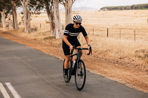 Young professional cyclist riding bicycle on countryside landscape. Fit sportswoman cycling outdoors.