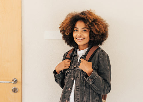 Portrait of a young woman with backpack at wall in high school