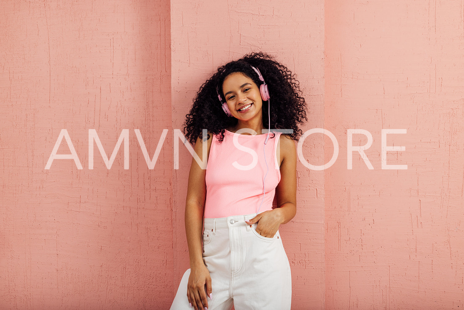 Beautiful smiling woman wearing bright casual clothes leaning pink wall listening to music