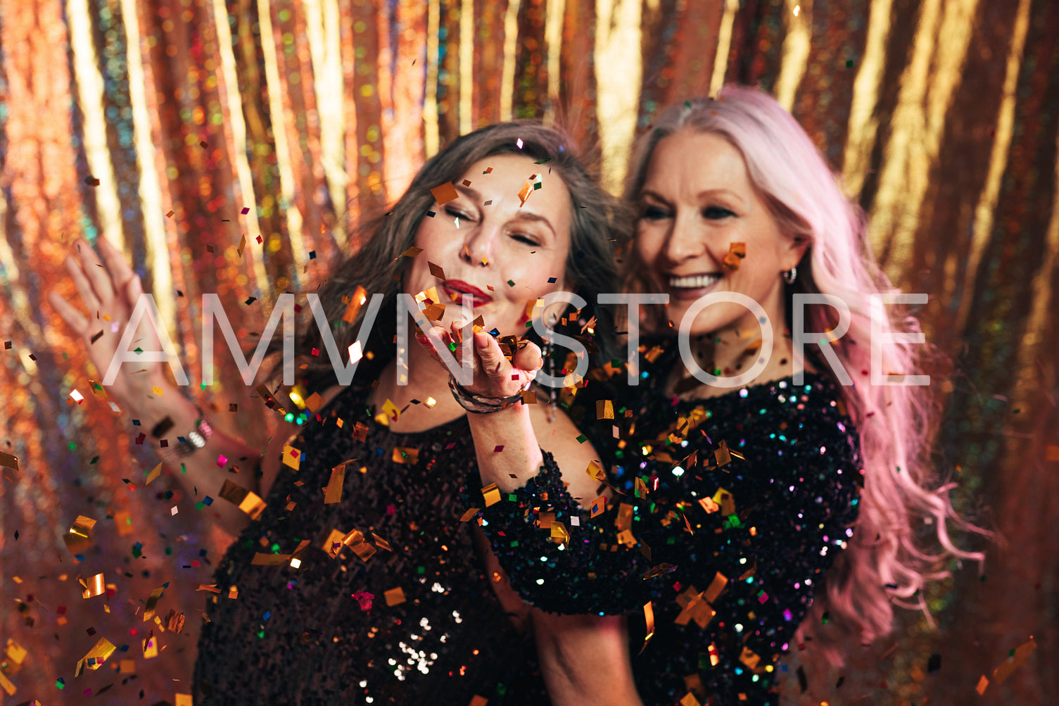 Two senior girlfriends having fun in studio blowing confetti