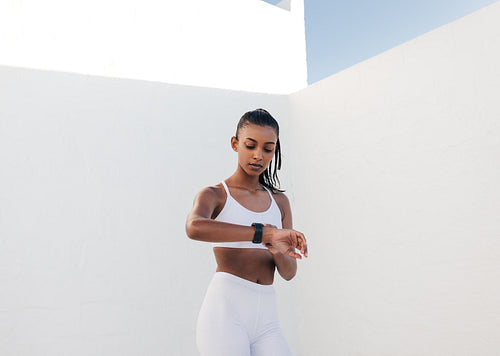 Young slim woman checking heart rate in the white outdoor studio. Fitness female looking at smartwatch checking pulse.