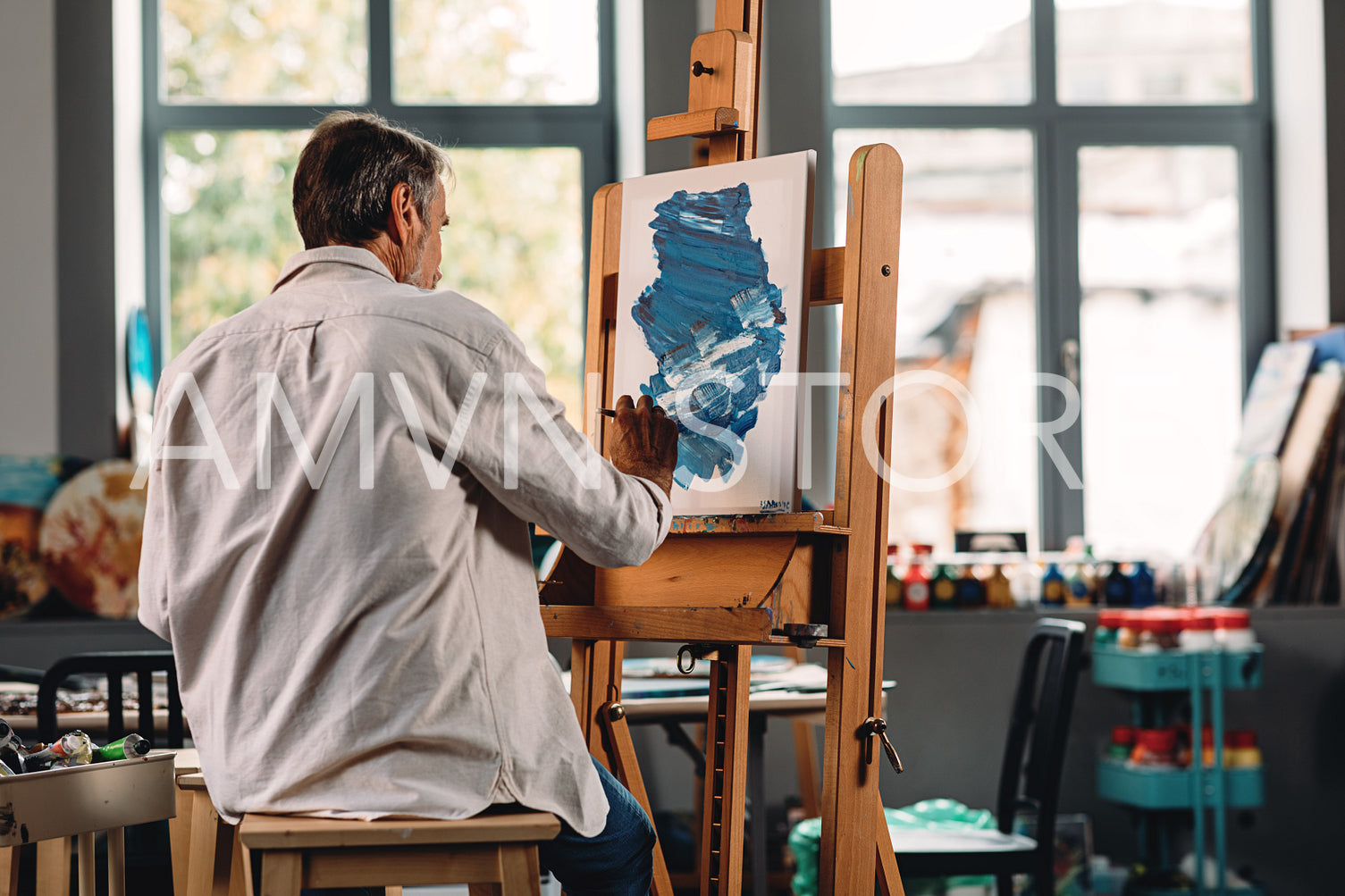 Back view of male painter drawing abstract picture on canvas while sitting in studio