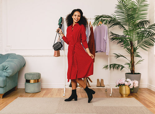 Beautiful smiling woman in studio posing in red dress at clothes rack