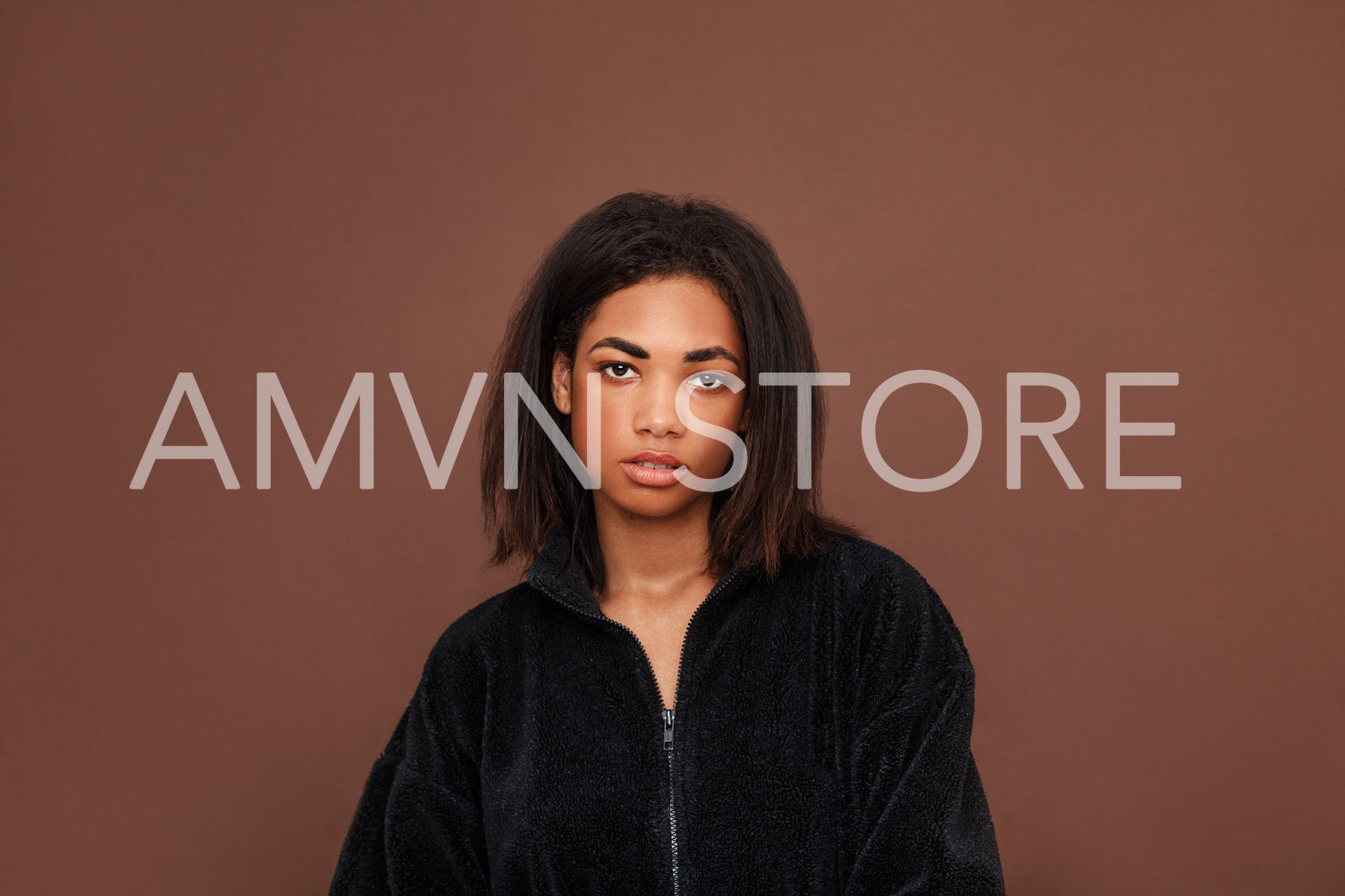 Beautiful young woman with black hair looking at the camera against a brown background