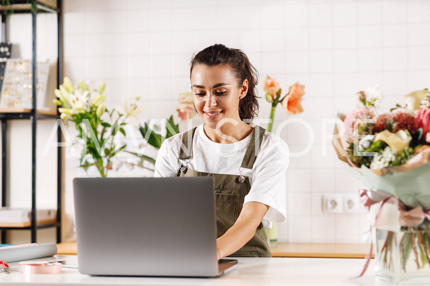 Woman wearing apron standing at the counter and working on laptop computer in a flower shop	