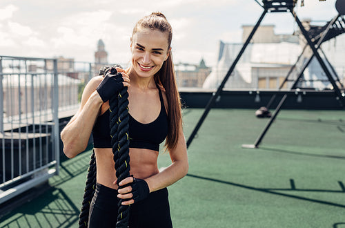 Smiling fitness woman holding battle ropes looking at camera after training