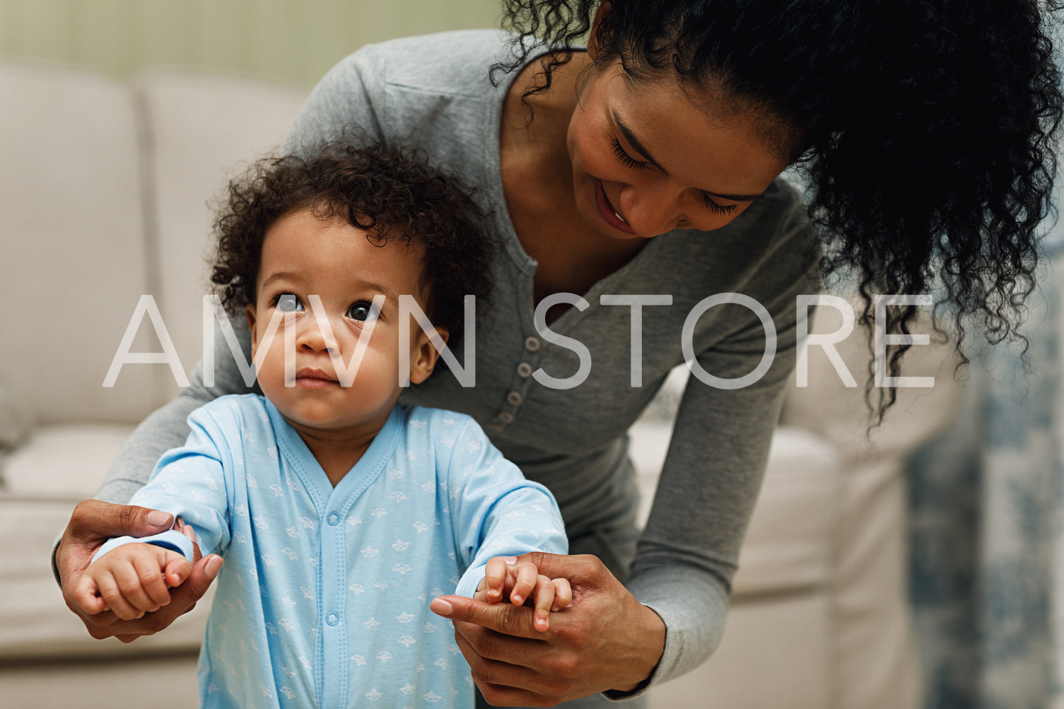 Mom helping toddler walk in living room. Young parent with son.	