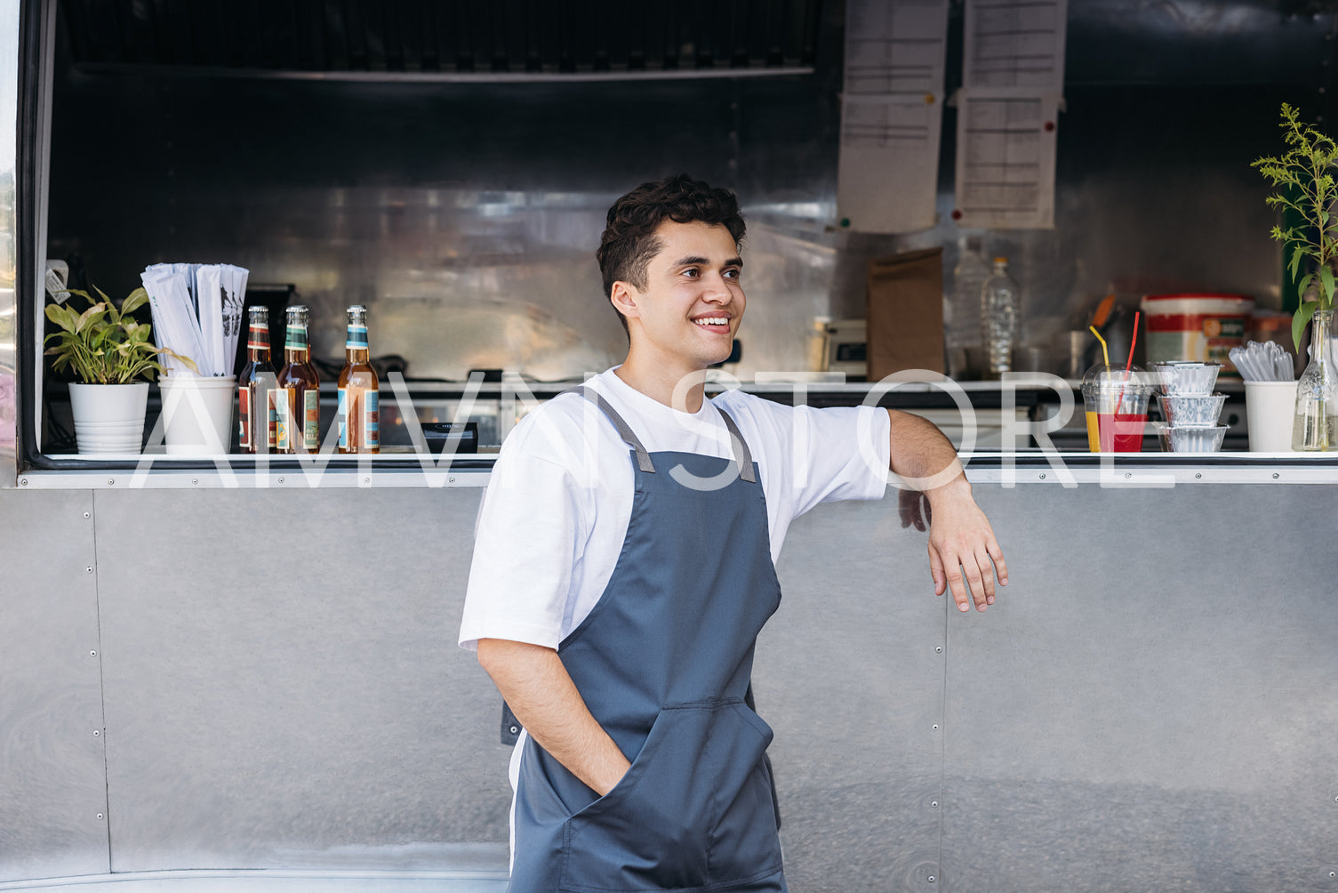 Side view of smiling waiter standing at food truck and looking away