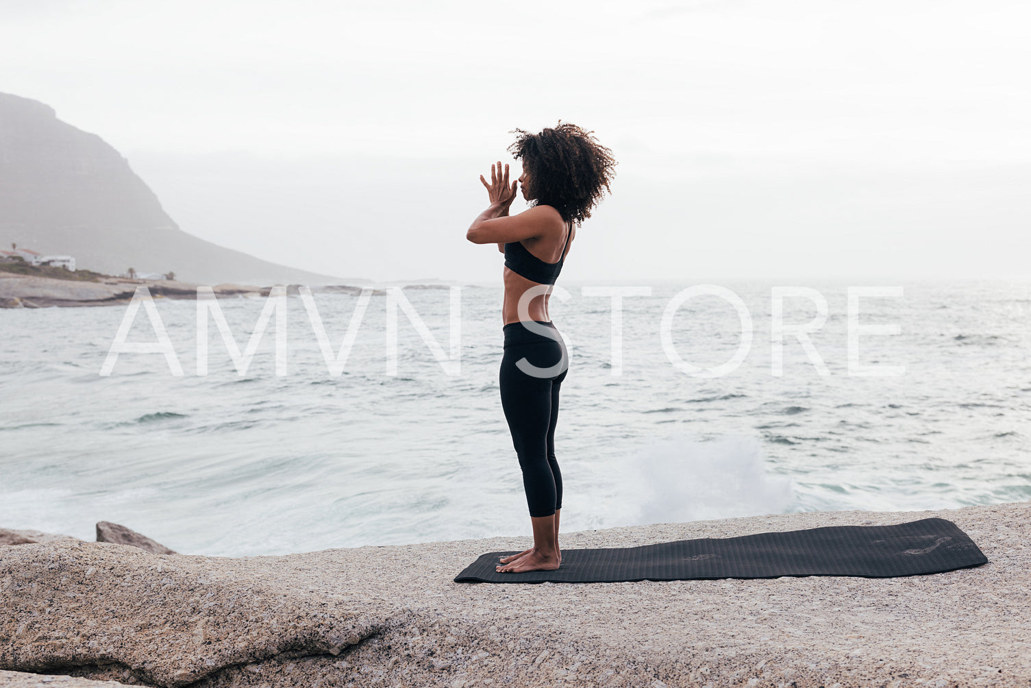 Full length of slim female standing with joined hands and meditating by ocean at evening