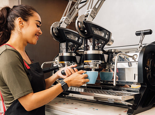 Female barista using a coffee machine. Smiling woman pouring hot coffee into cup at cafe.