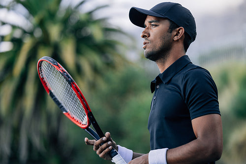 Side view of a young tennis player with racket looking away