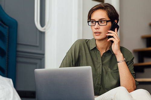 Woman entrepreneur on business trip working from hotel room sitting on a bed