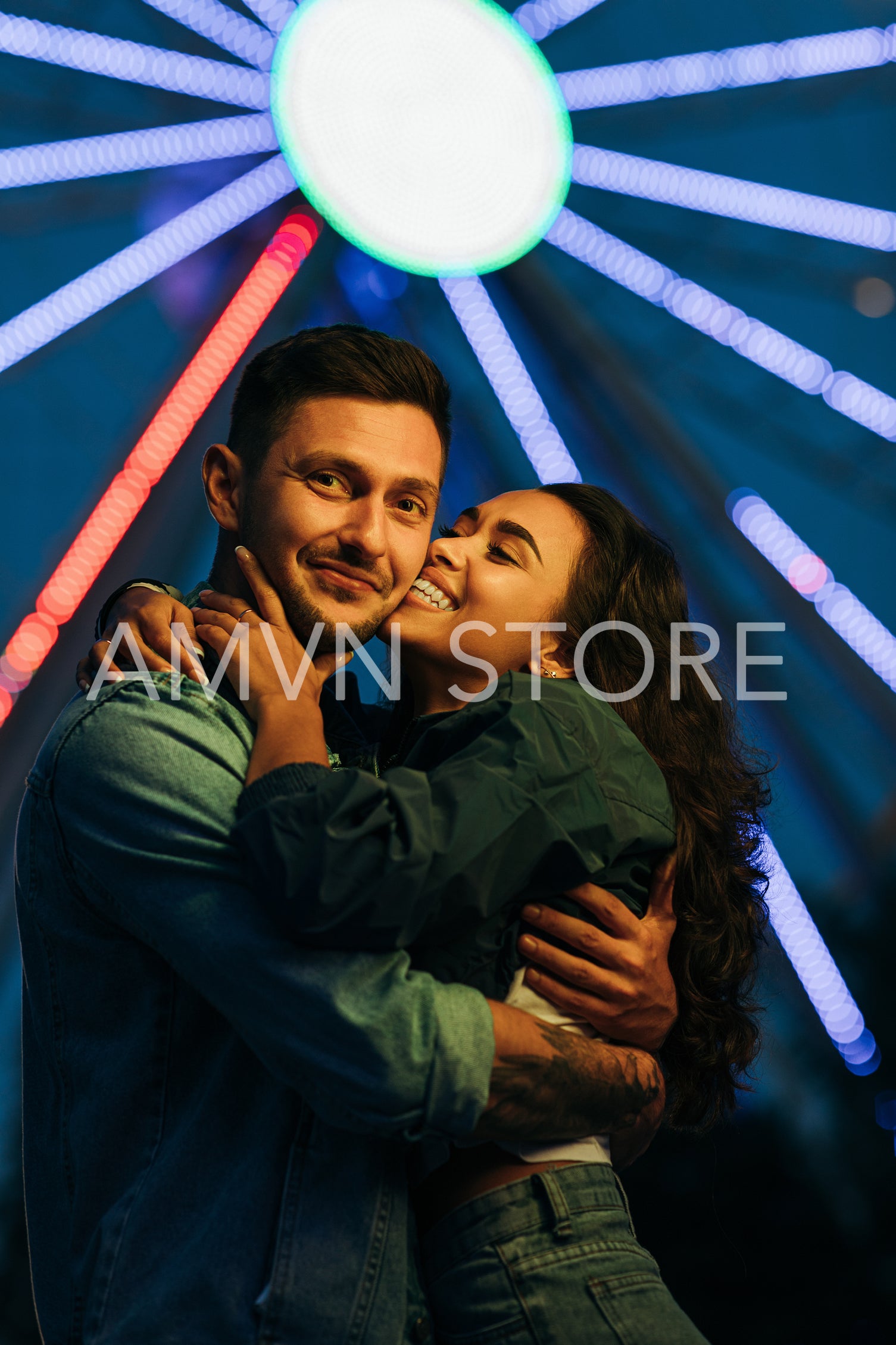 Young couple hugging and kissing against colorful lights from ferris wheel