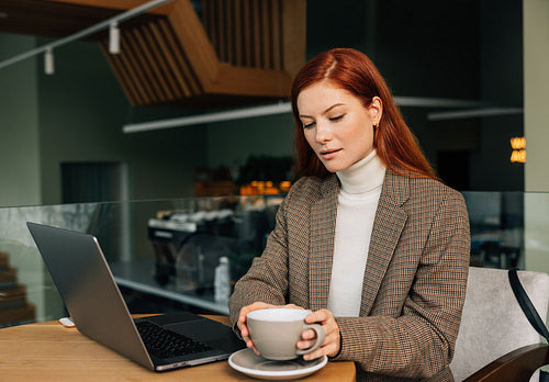 Young female entrepreneur in a cafe in morning. Woman with ginger hair working from a coffee shop.