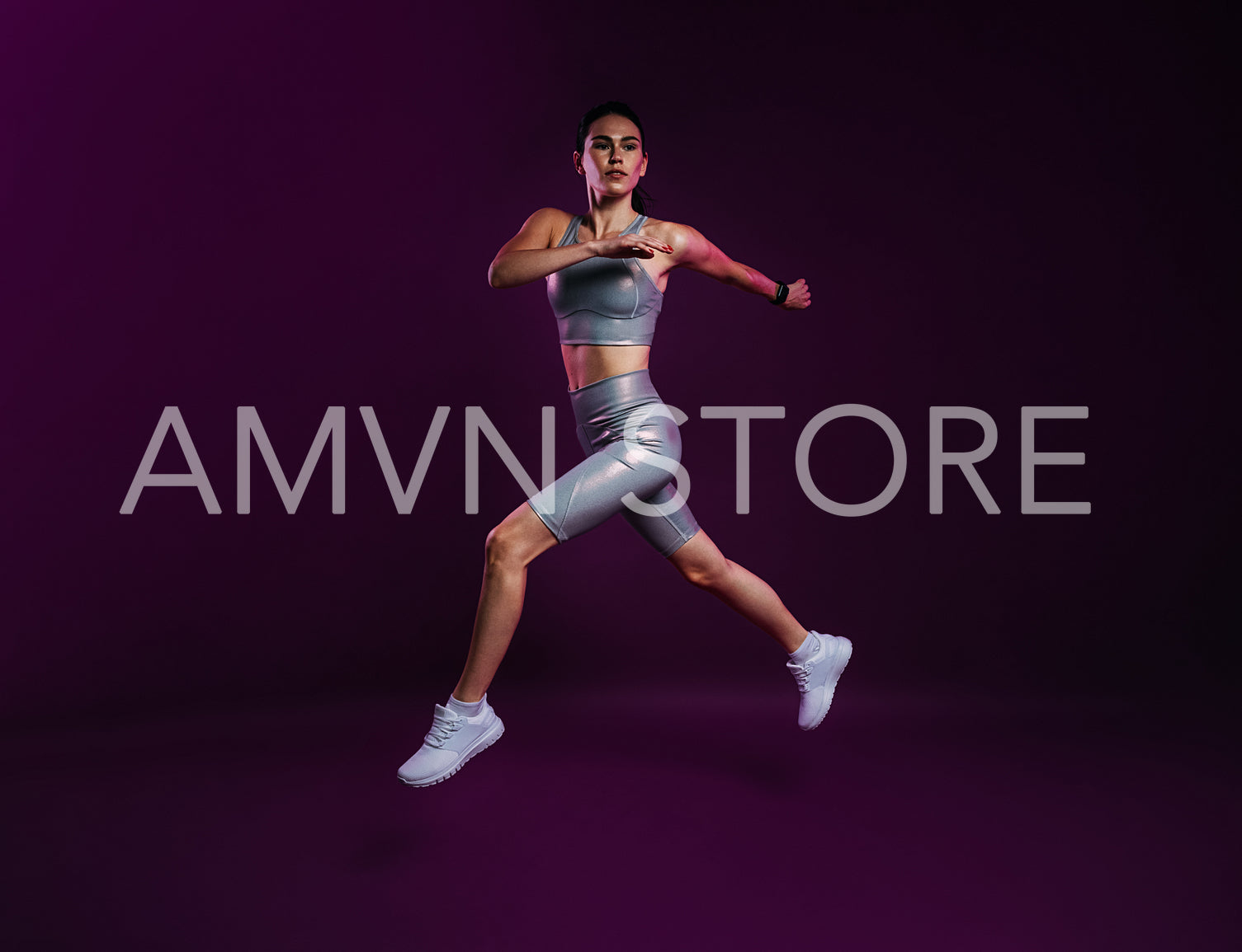 Full length of slim woman in silver sports clothes running and jumping over a magenta backdrop