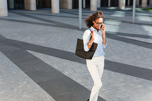 Modern businesswoman talking on mobile phone while walking on a street