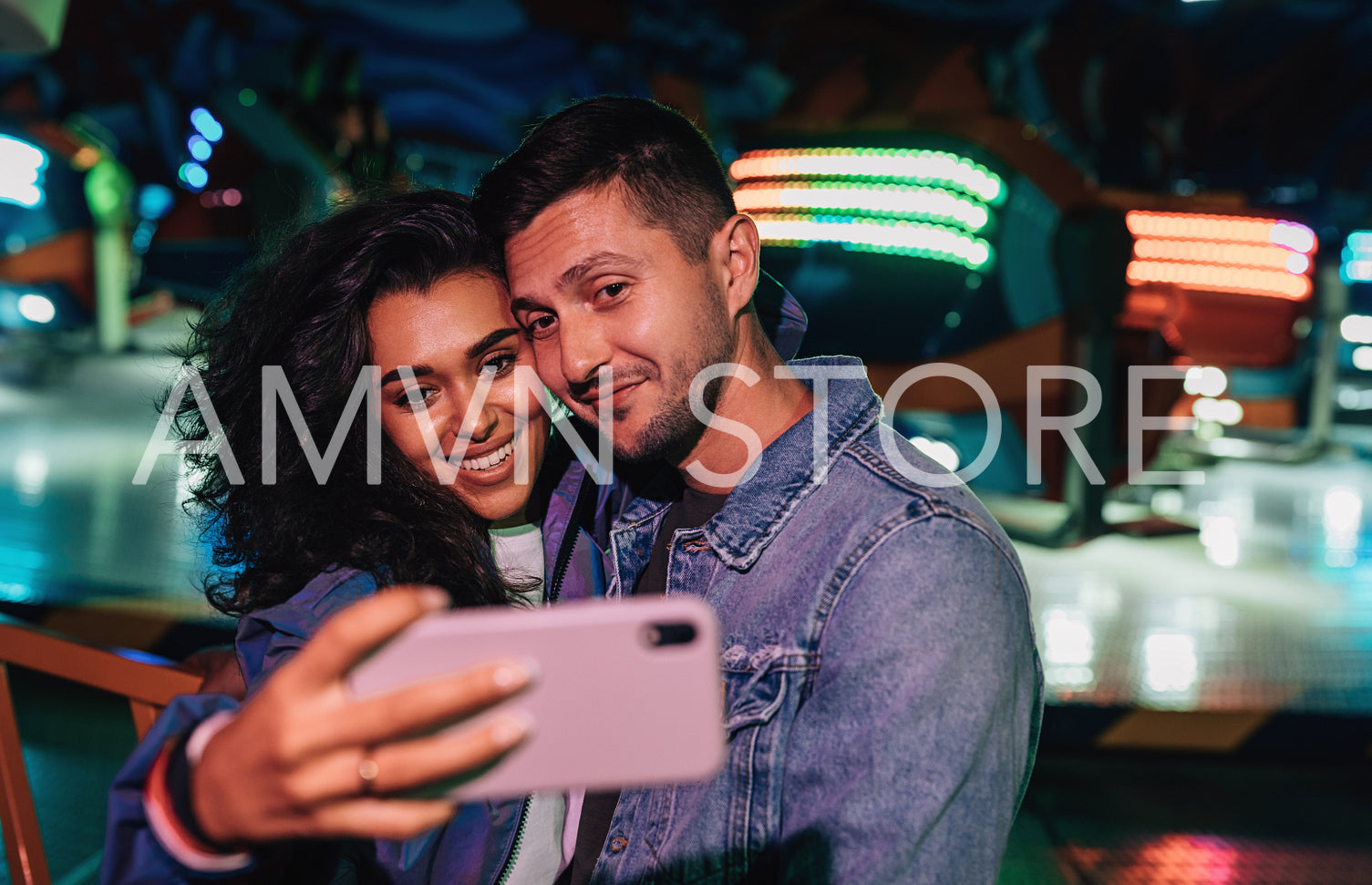 Young couple making selfie in amusement park against colorful lights