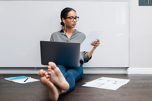 Female entrepreneur sitting on floor at home with document and using laptop