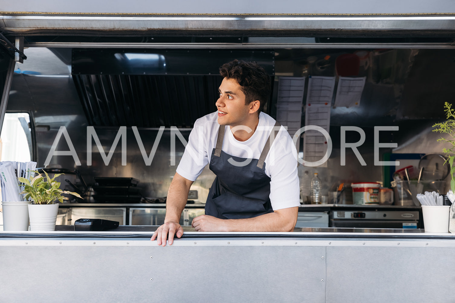 Businessman in apron leaning on a counter of his food truck looking away while waiting for customers