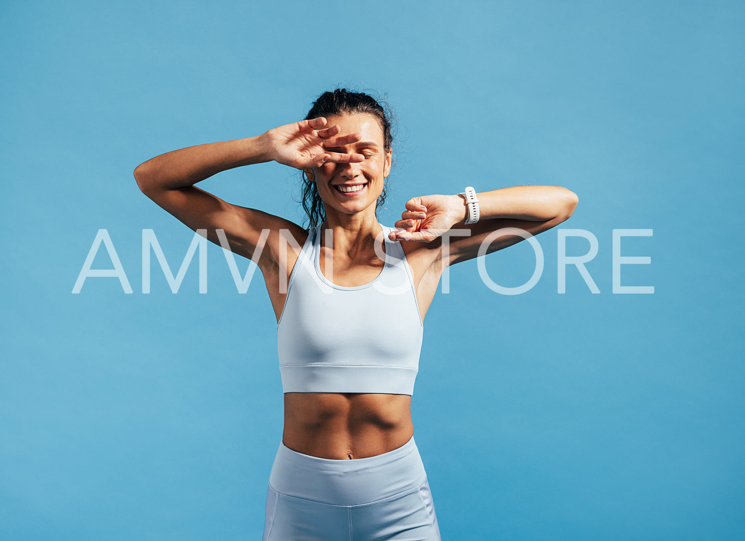 Happy fitness woman relaxing after training. Young female in sports wear hiding face with hands on blue background.