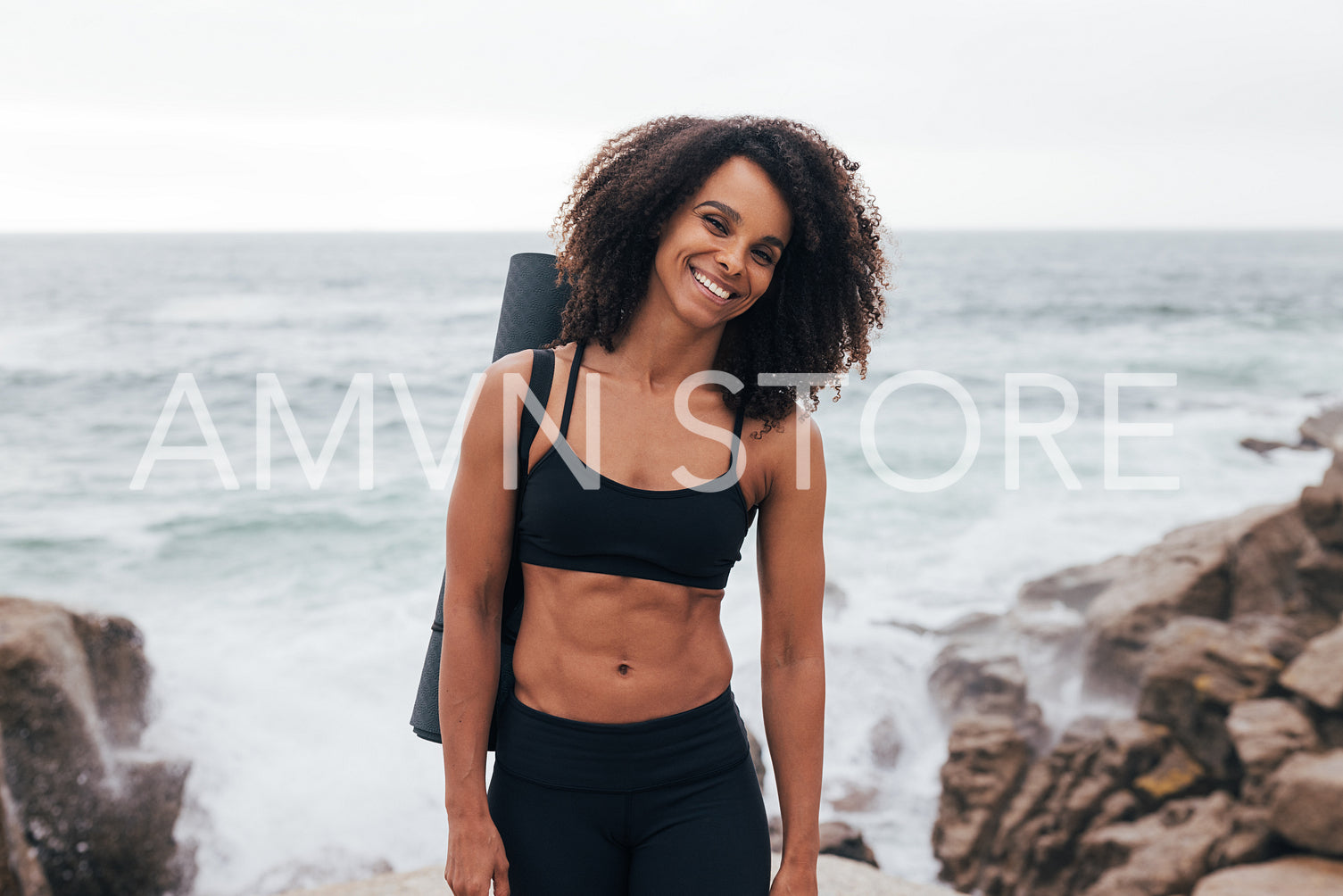 Portrait of a young sportswoman with mat looking at camera while standing by coast