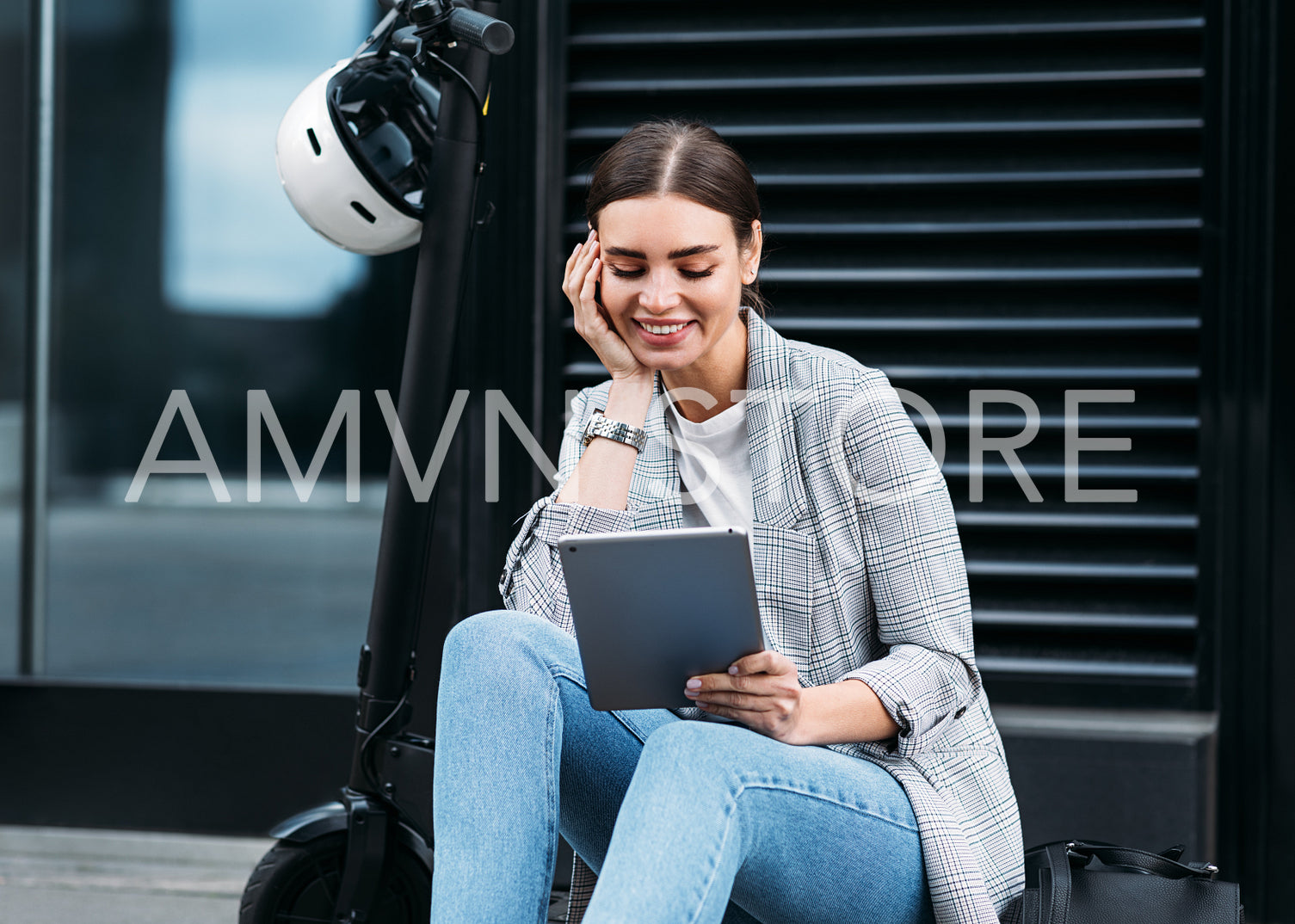 Cheerful woman looking at a digital tablet while sitting on electric scooter near an office building