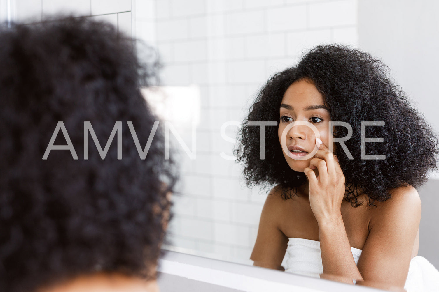 A young woman looking at mirror and examines her skin, touching face with finger	