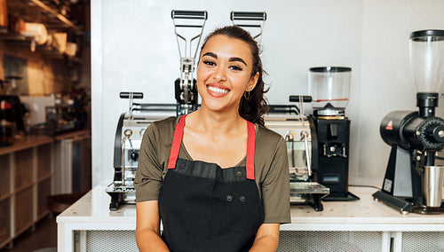 Happy waitress standing at coffee machine and looking at camera