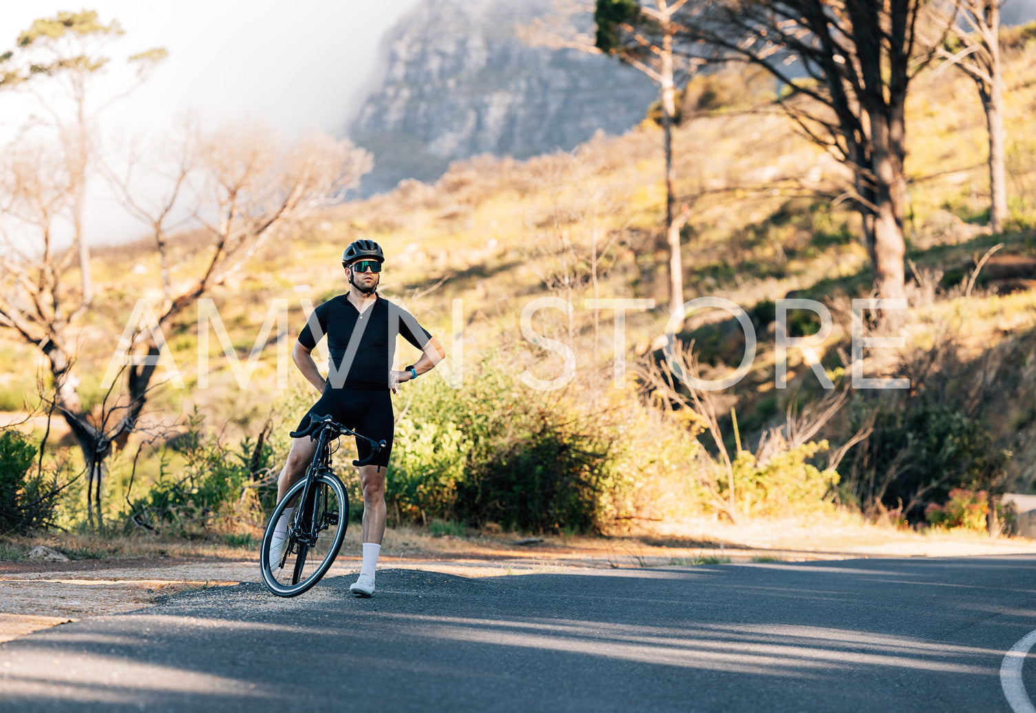 Professional cyclist in black sportswear relaxing on a roadside with hands on a hips