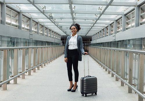 Smiling woman standing with suitcase in a center of corridor in transportation terminal