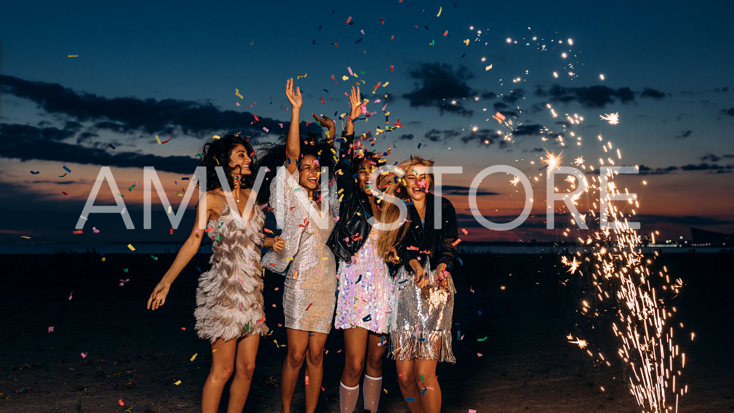 Four women celebrating at sunset. Happy female friends dancing between fireworks at dusk.	