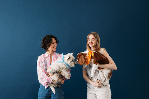 Two women holding their dogs in studio. Females with cute little