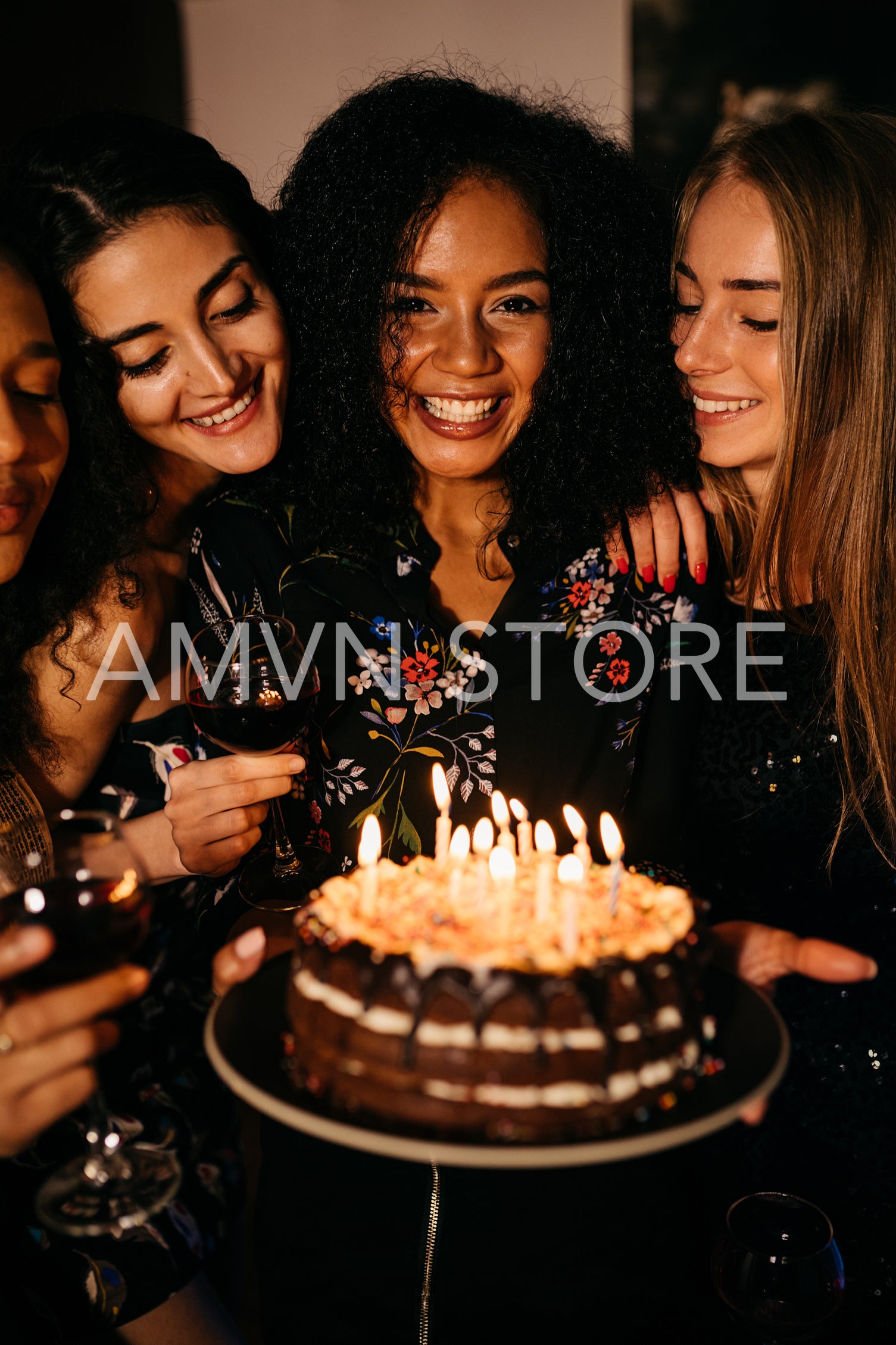 Young happy woman holding a birthday cake, standing indoors surrounded by girlfriends	