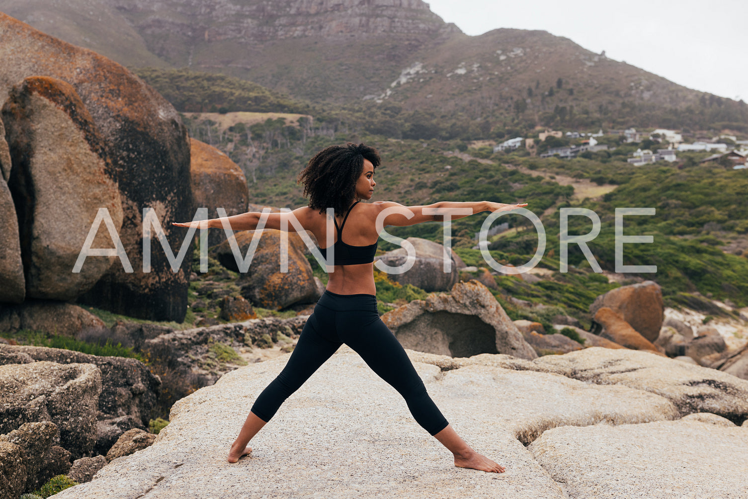 Barefoot woman practicing yoga exercises outdoors while standing on a big rock