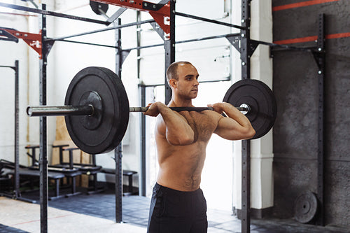 Shot of muscular young man doing squats with barbell in a gym