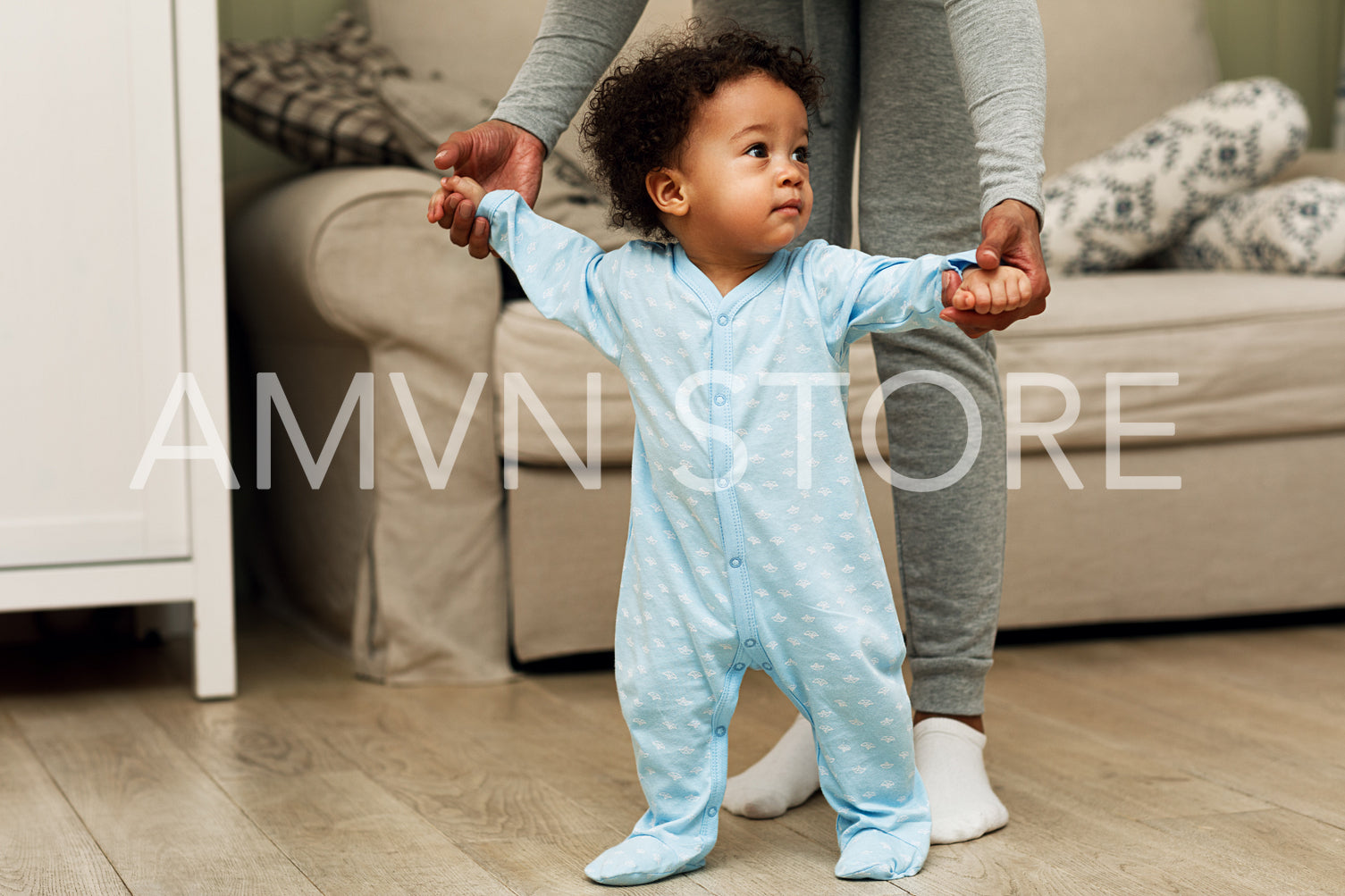 Mother teaching baby boy to walk in a room. Woman holding hands of her son.	