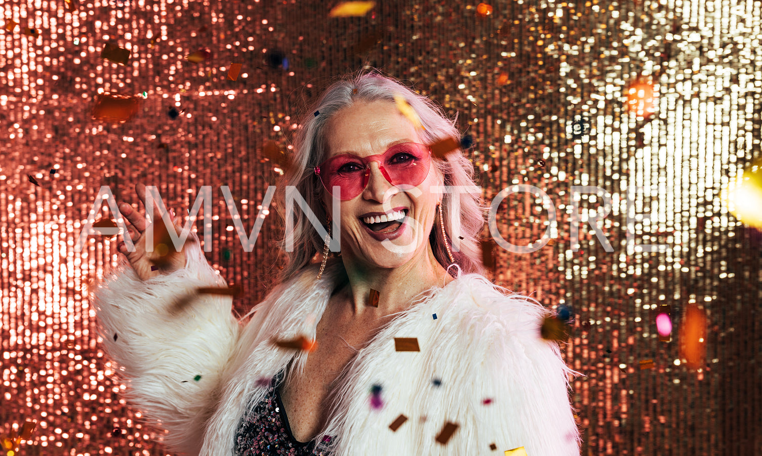 Laughing woman in white fur coat throwing confetti in studio aga