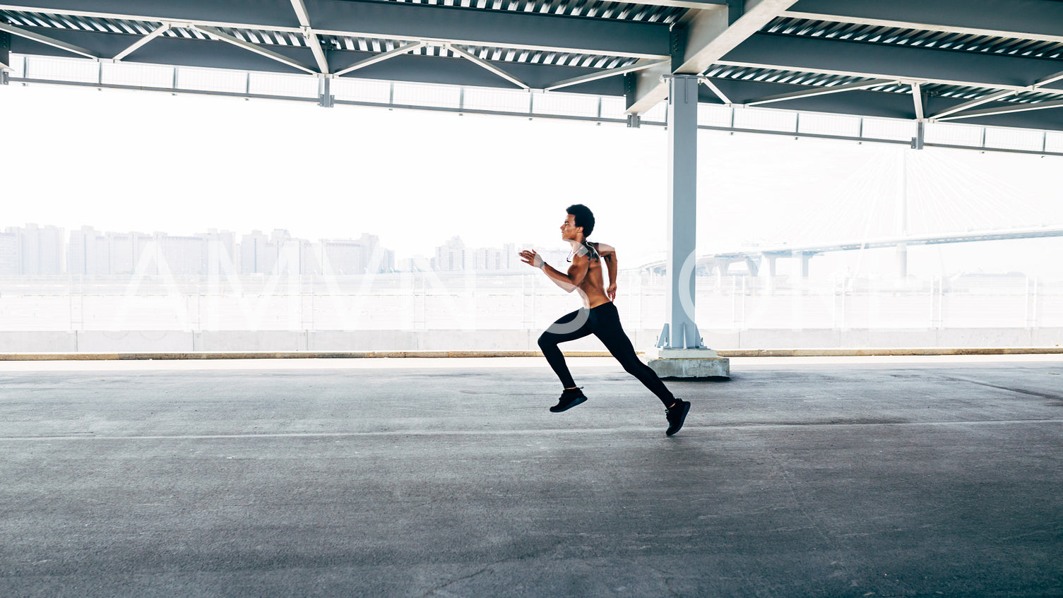 Athlete running outdoors. Young sportsman with bare chest exercising near a bridge.	