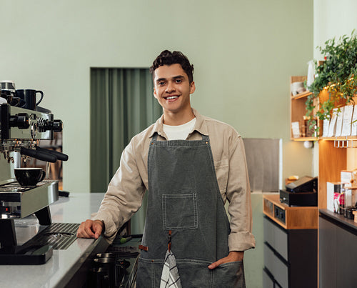 Smiling male barista in an apron looking at camera in a cafe