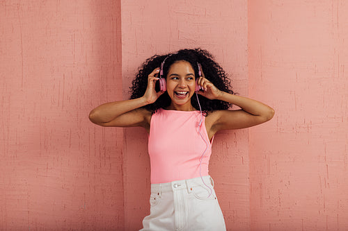 Beautiful woman with curly hair listening to music by pink headphones wearing casual clothes having fun