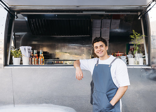 Handsome waiter leaning on a food truck. Young business owner waiting for customers.