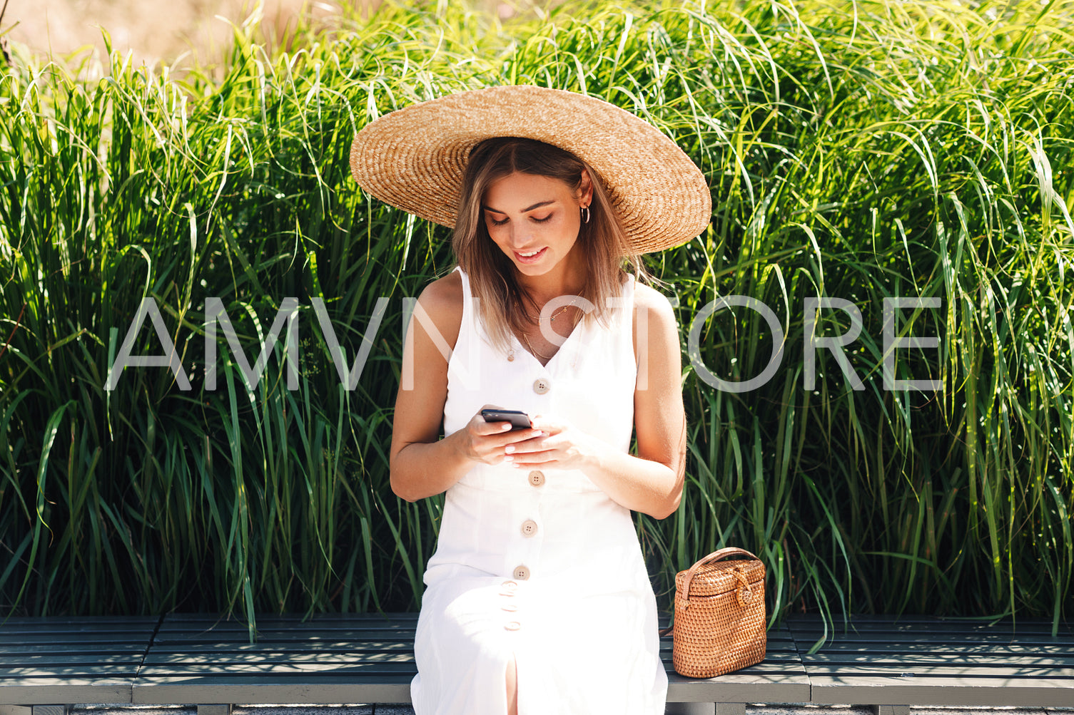 Stylish woman wearing straw hat and using mobile phone while sitting in park	