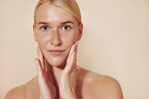 Female with freckled skin touching her face. Portrait of a beautiful blond woman looking at the camera and massaging her face.