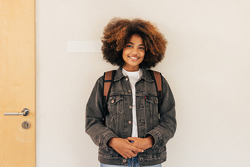 Teenage girl in casuals standing at wall in school and looking at camera