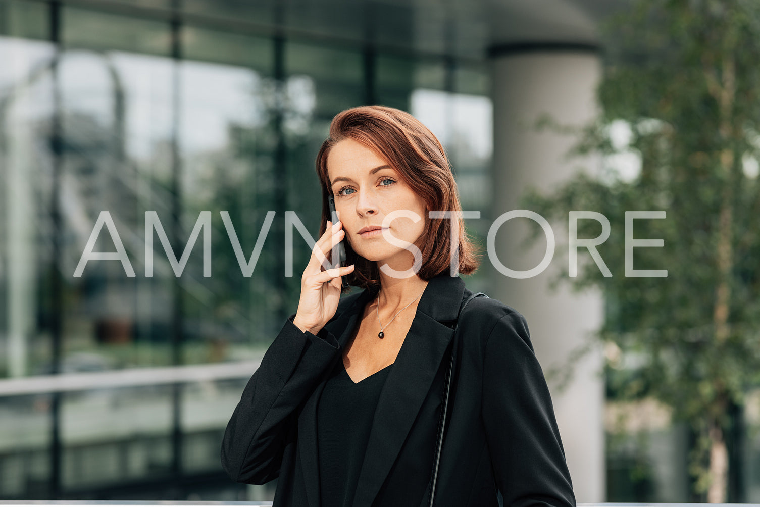 Confident businesswoman with ginger hair talking on a mobile phone. Middle aged female in black formal clothes talking on a cell phone outdoors.