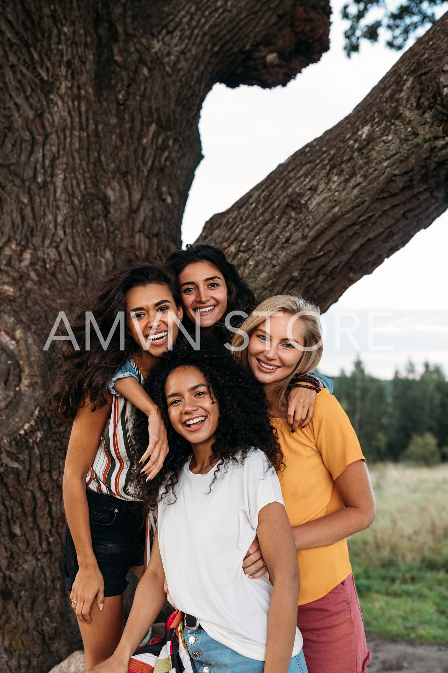 Group of young diverse women standing in front of a big tree and looking at camera