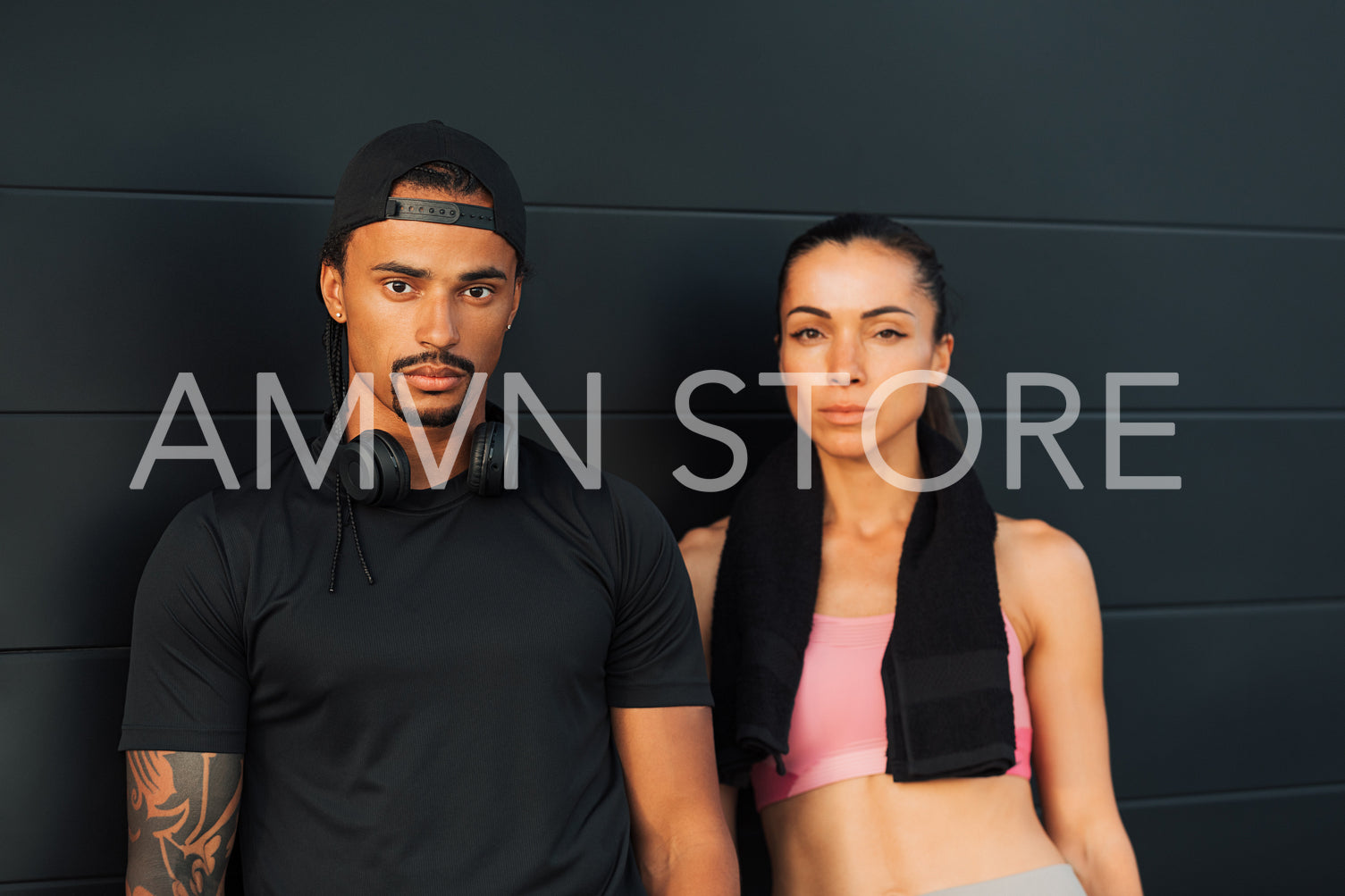 Couple in fitness wear relaxing at a black wall. Man and woman in sportswear looking at camera after a workout.